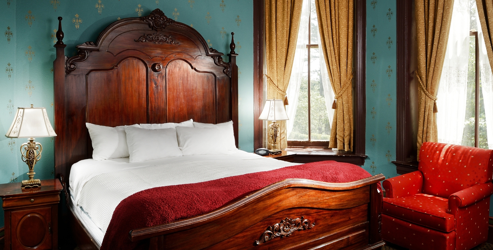 a bed with a red blanket and a lamp in front of a window