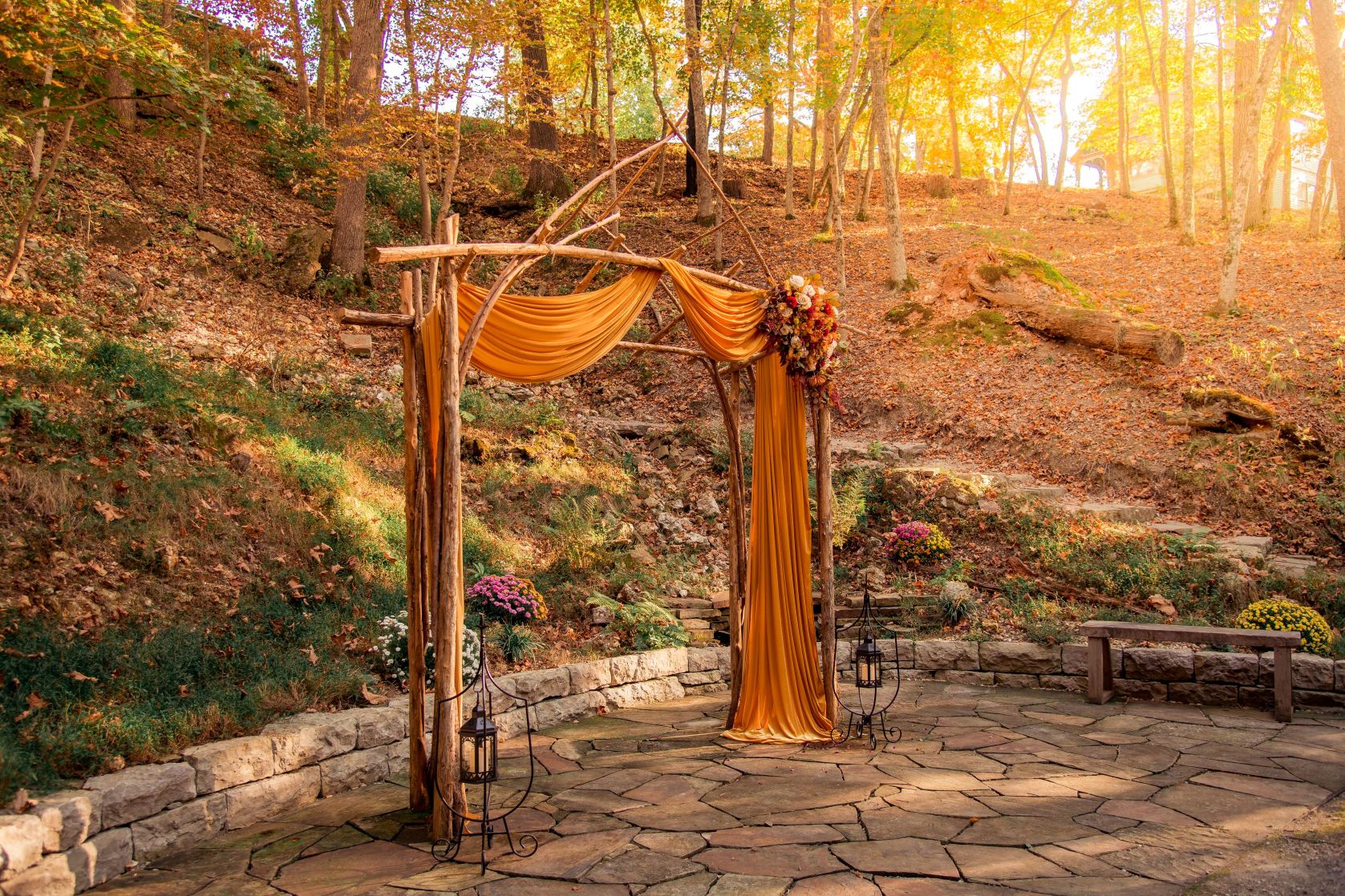 a wooden arch with a cloth and flowers on a stone patio