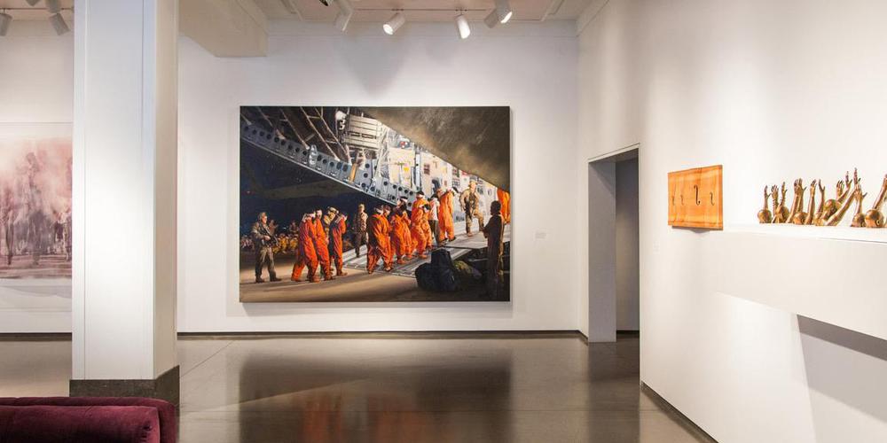 a painting of people in orange jumpsuits on a white wall