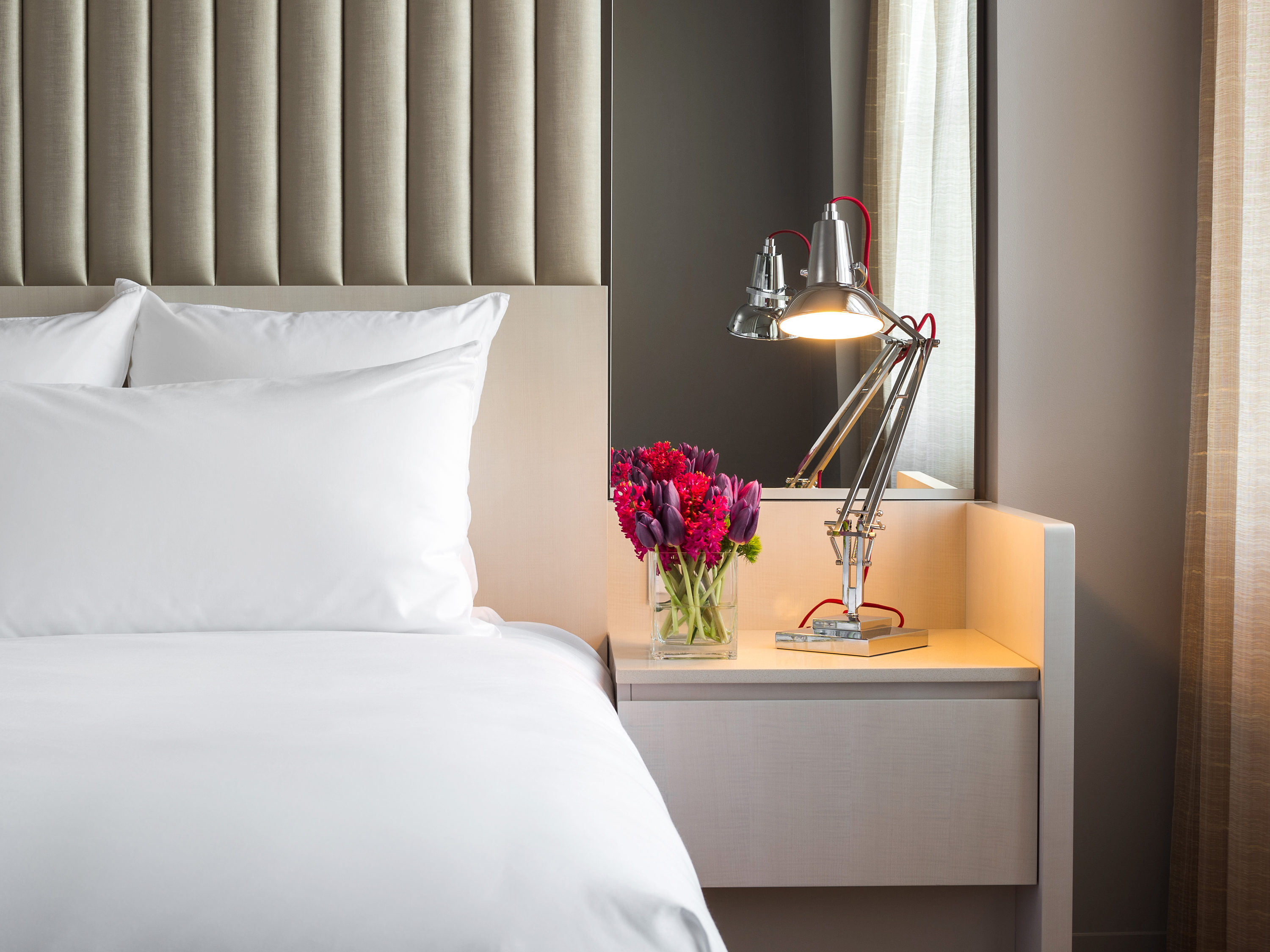 a bed with a lamp and flowers on a table