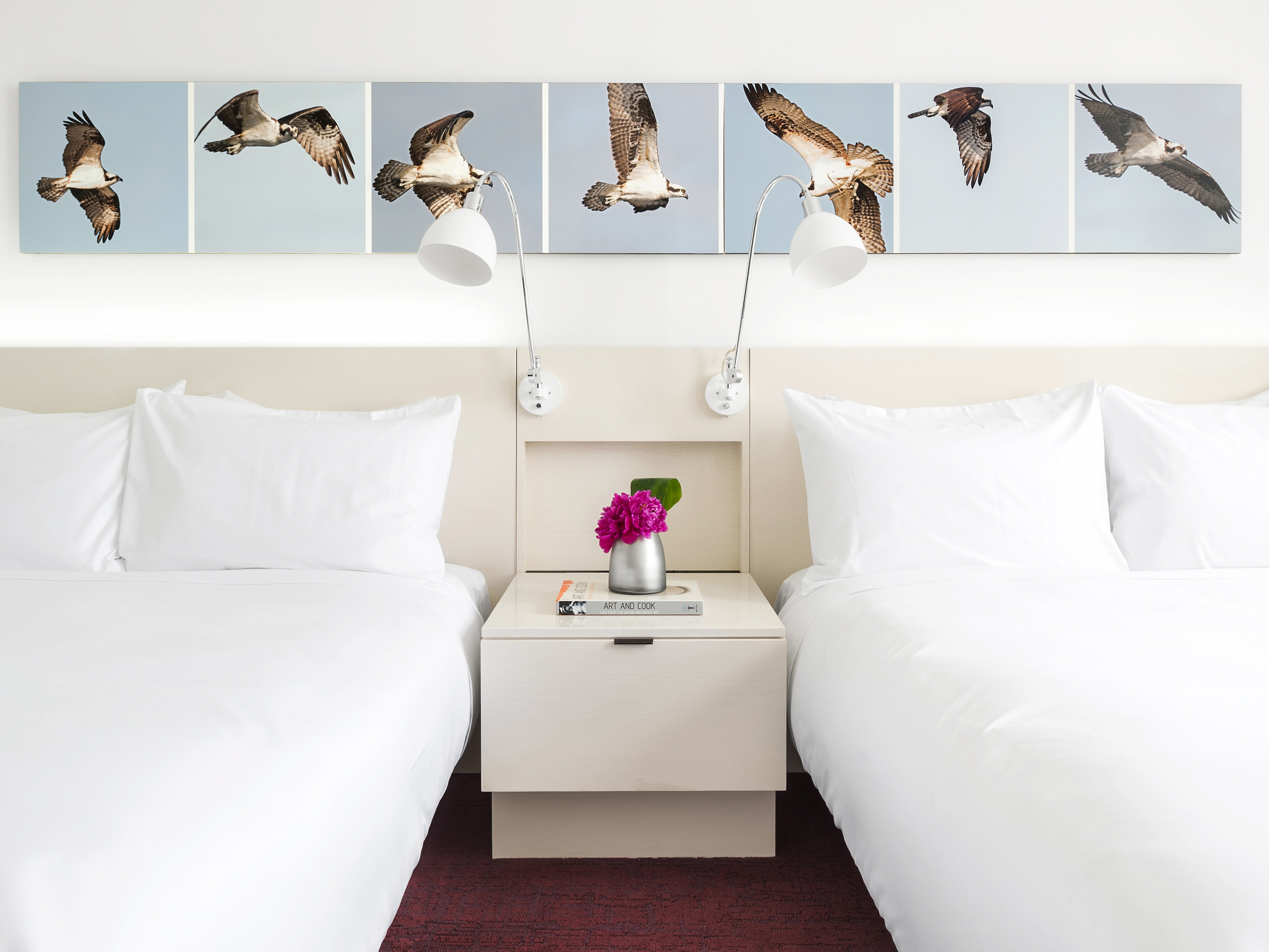 two beds with white pillows and a vase of flowers on a table