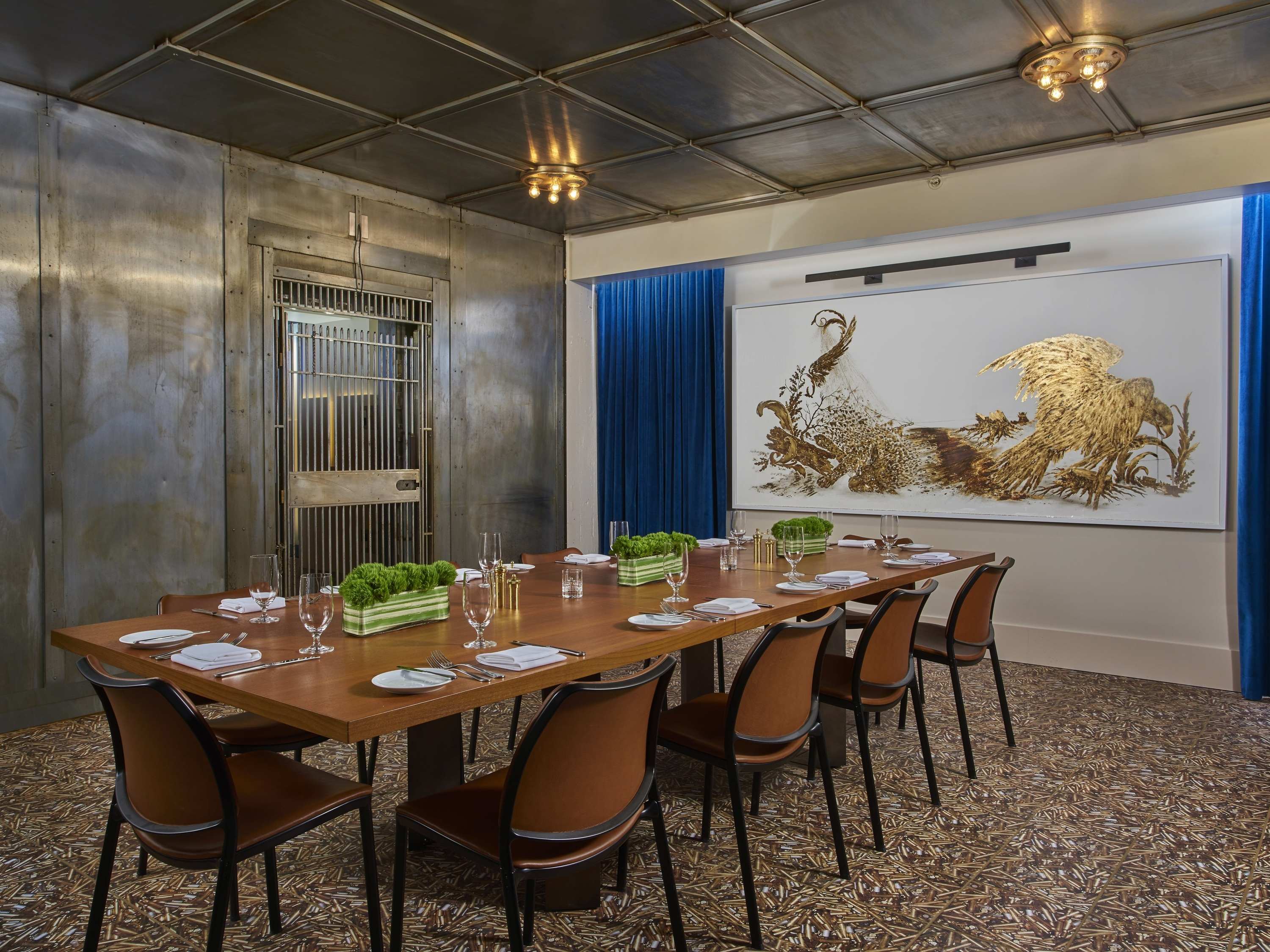 a long table with plates and glasses in a room with a large picture on the wall