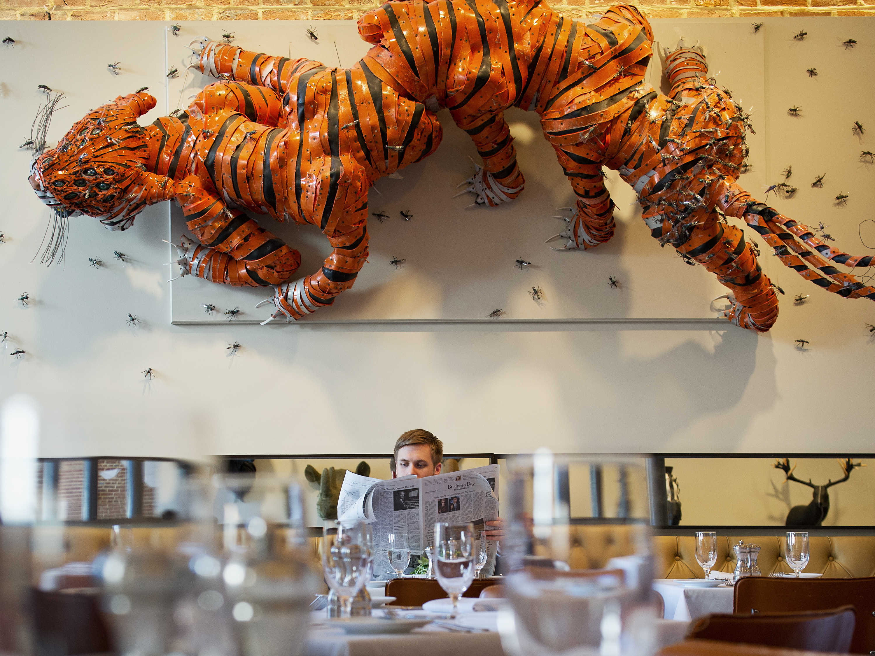 a man reading a newspaper in front of a wall of orange tigers