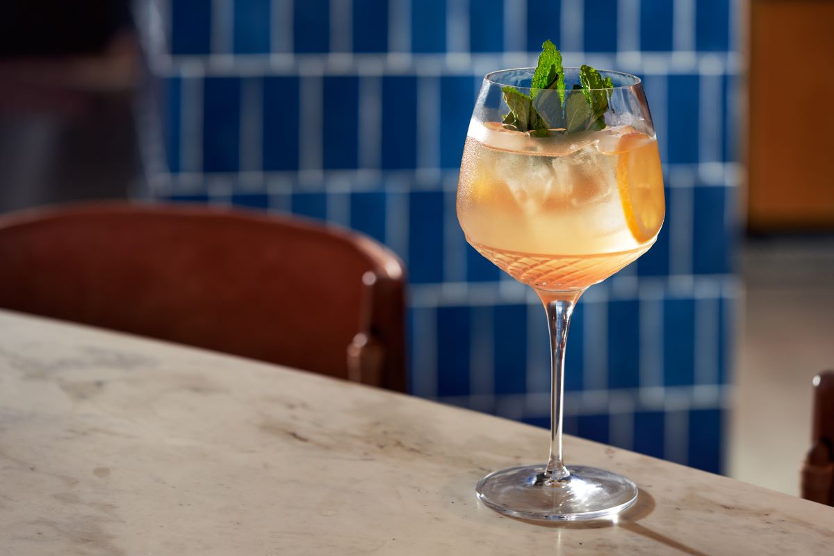 a glass of drink with orange and mint leaves