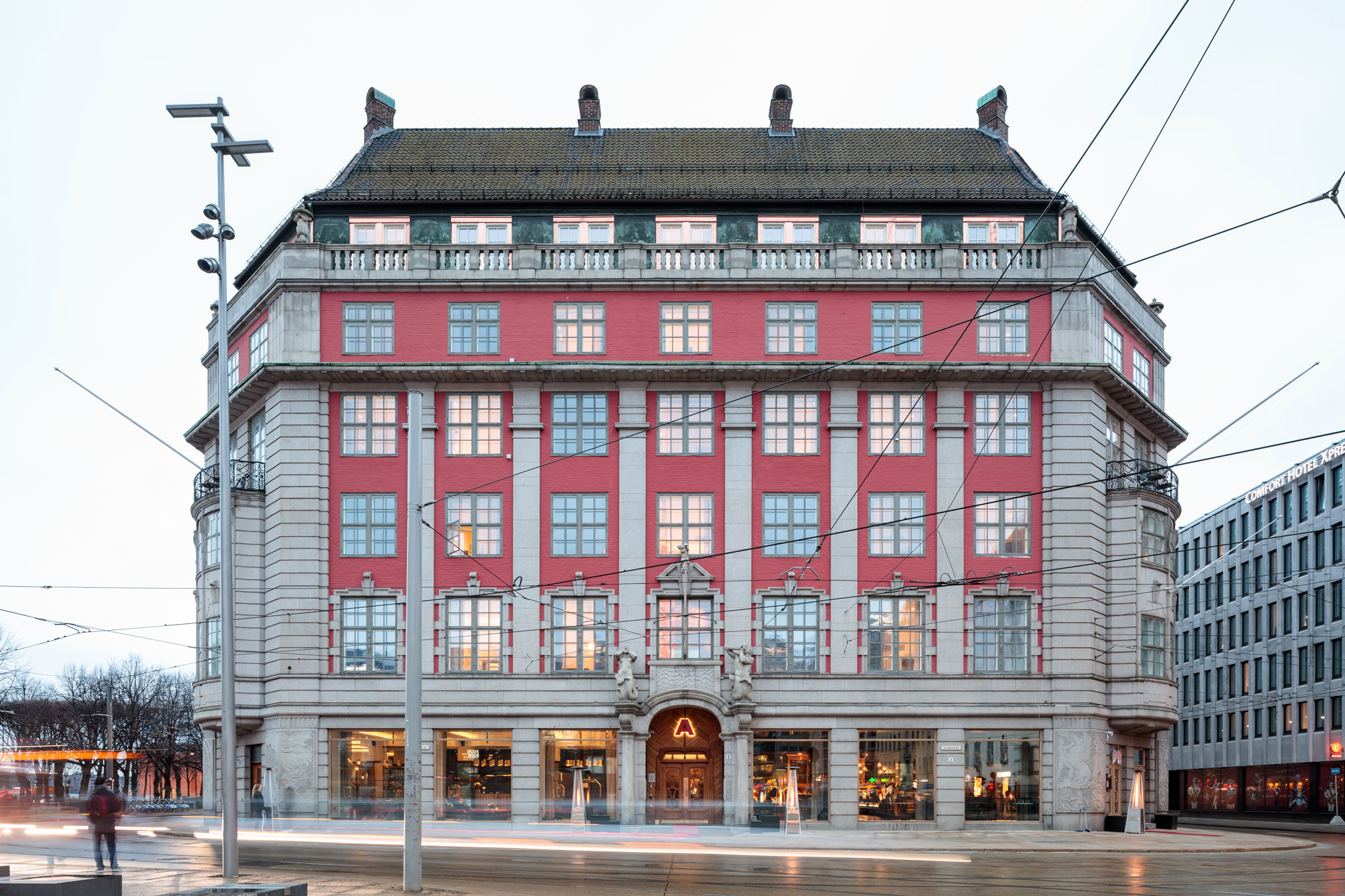 Exterior facade of a grand, multi-story hotel building featuring a striking red brick and stone stone exterior, stone columns, large windows, and a prominent arched entrance.