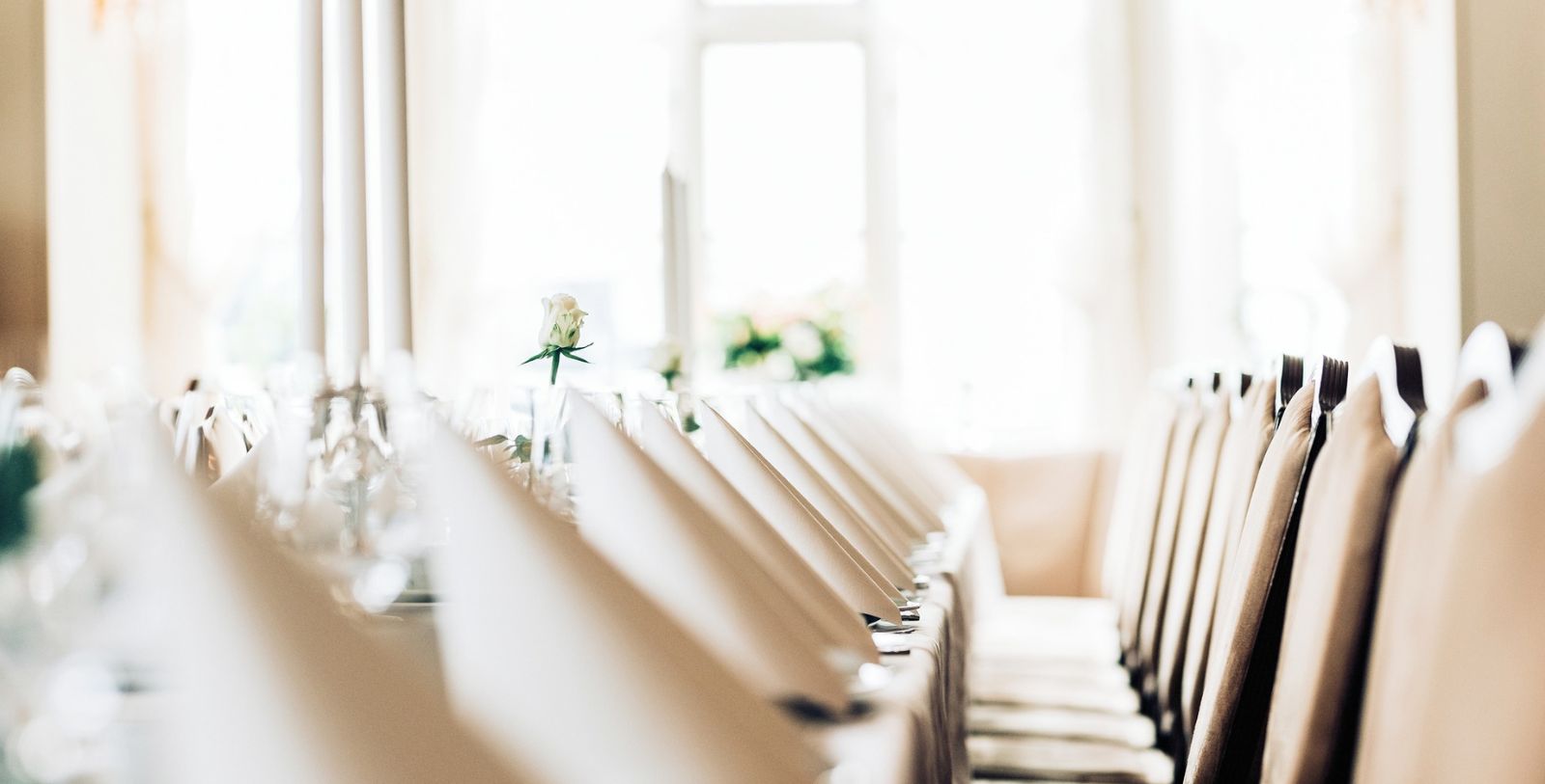 a row of chairs with white cloths and a flower in a glass vase