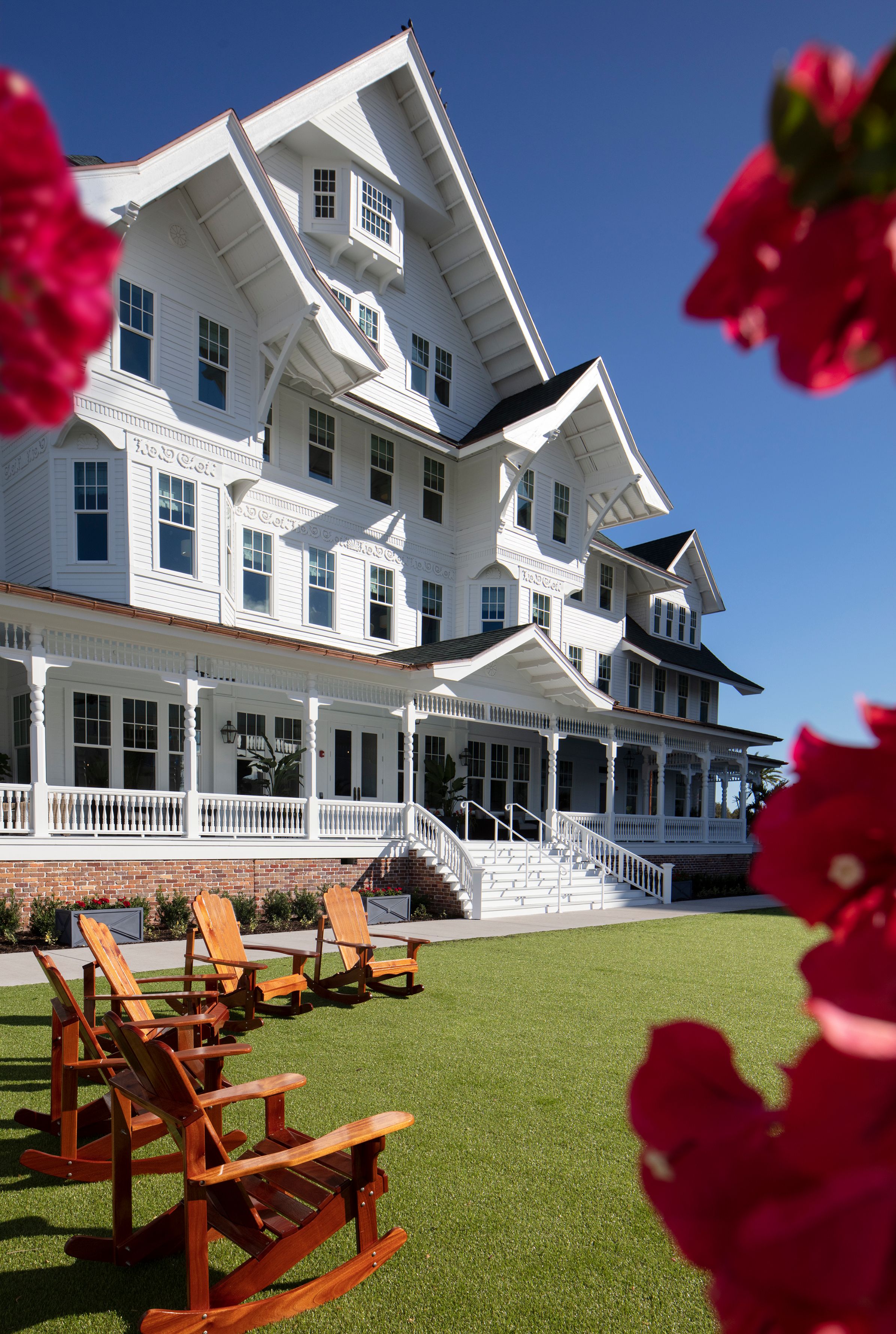 a large white house with lawn chairs and red flowers