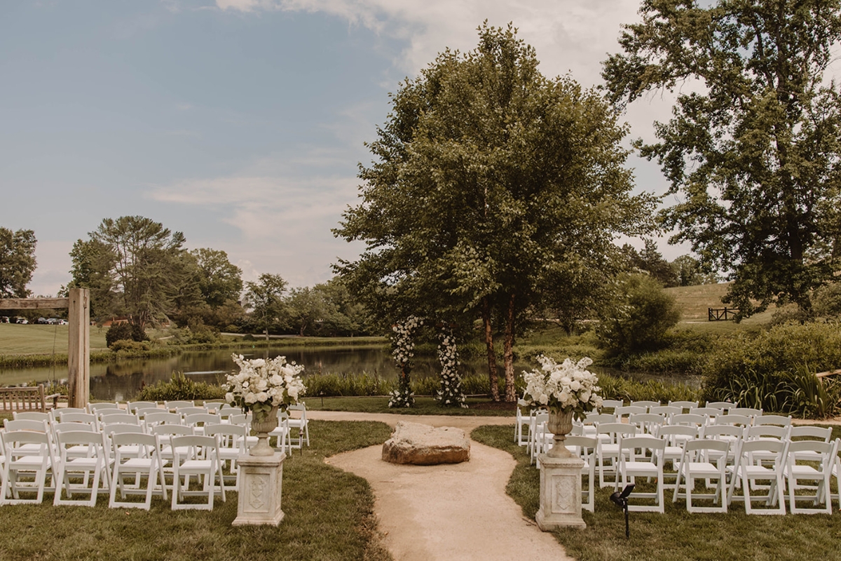 a wedding ceremony with white chairs and a tree