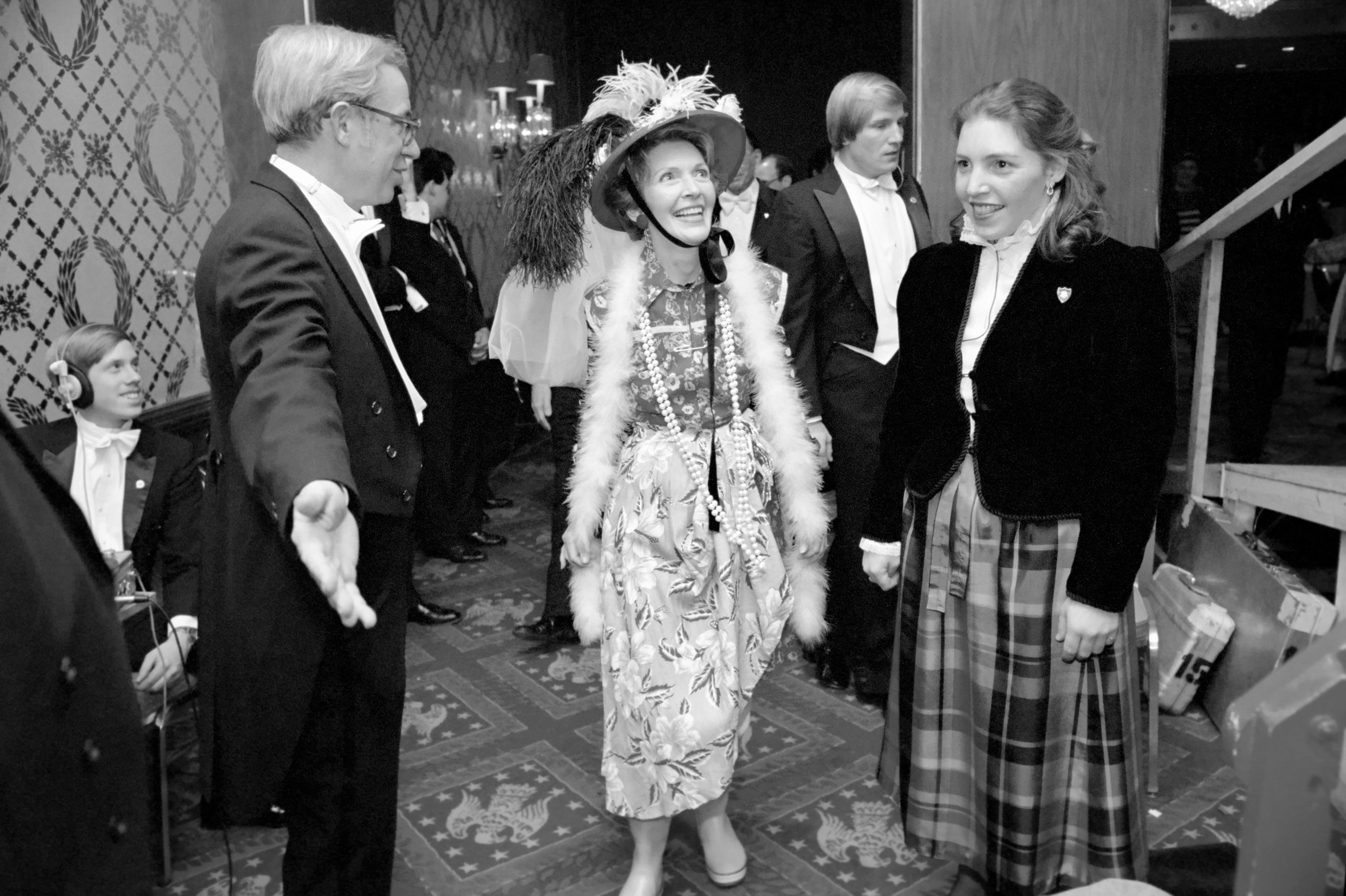 a woman in a dress and hat with a woman in a dress and a man in a suit