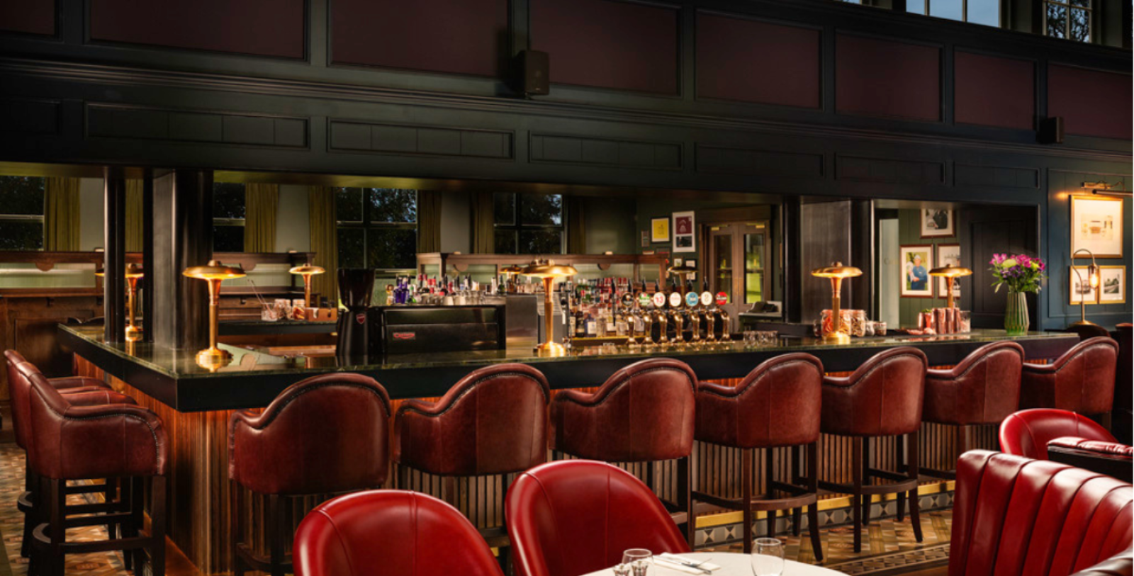 a bar with red chairs and a row of tables