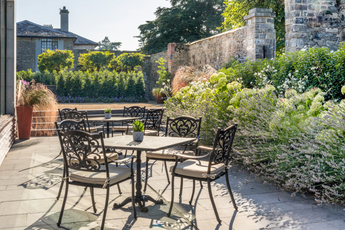 a table and chairs outside with a stone wall and bushes