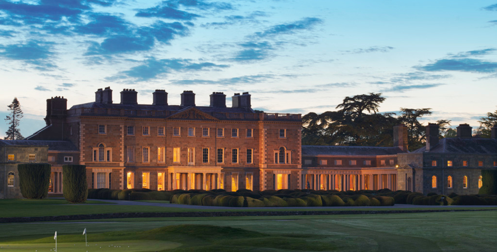 a large building with a lawn and trees in the background