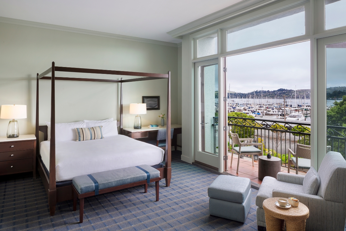 a room with a bed and chairs and a balcony overlooking a marina