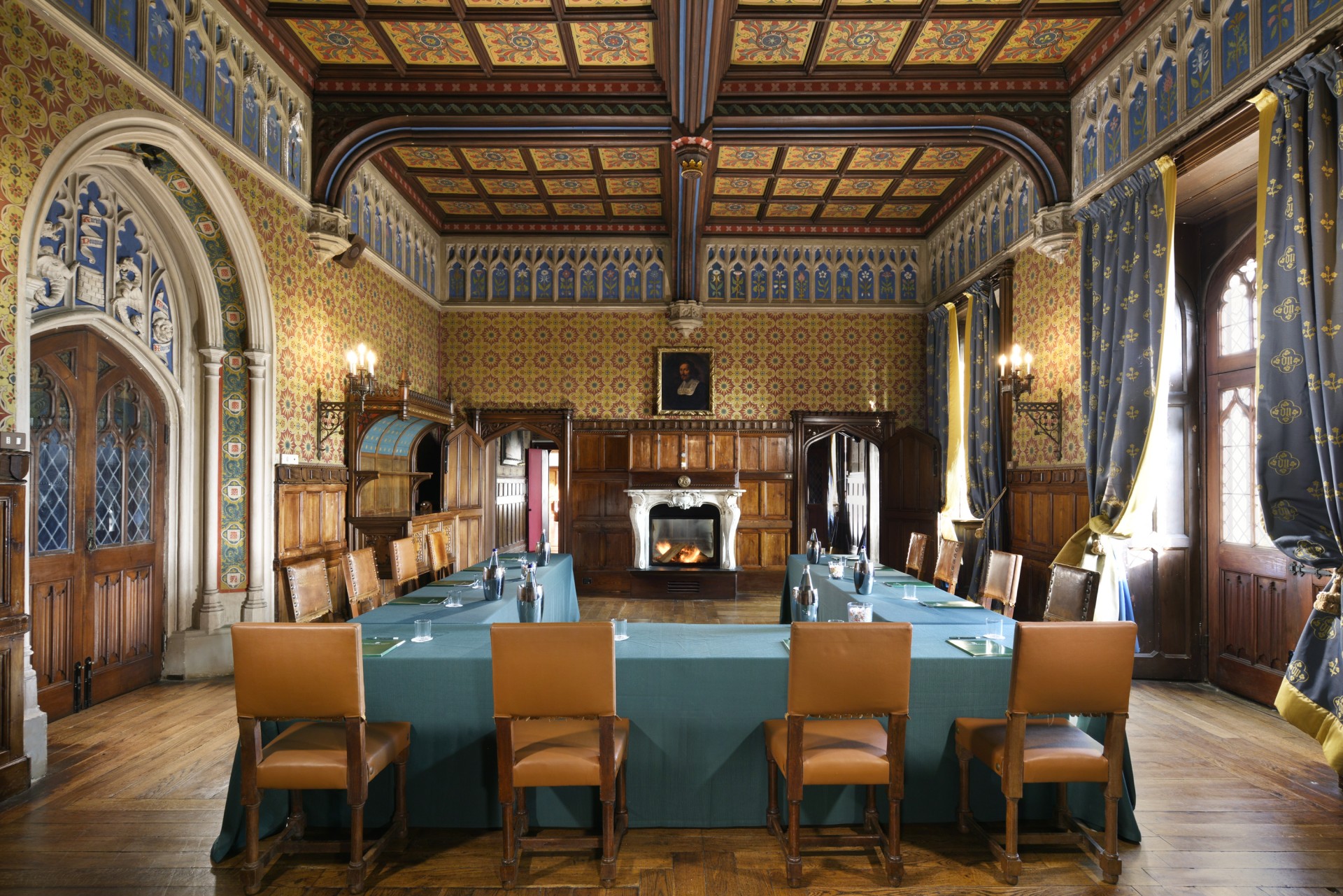An opulent, Gothic Revival meeting room set up with a U-shaped conference table, featuring intricate painted coffered ceilings, ornate wall paneling, a grand fireplace, and leather chairs.