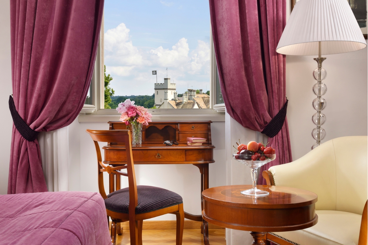 a room with a desk and chair and a table with a vase of fruit