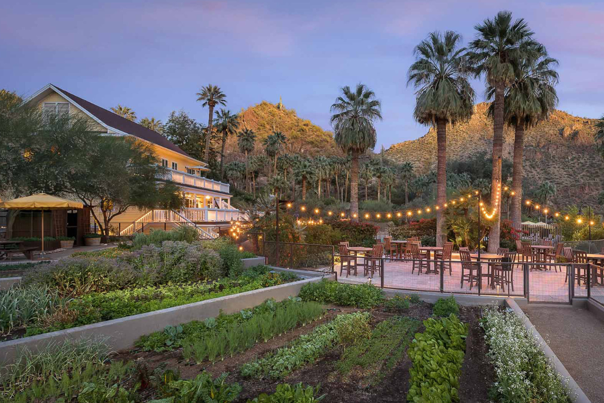 a garden with a patio and a building with trees and mountains in the background
