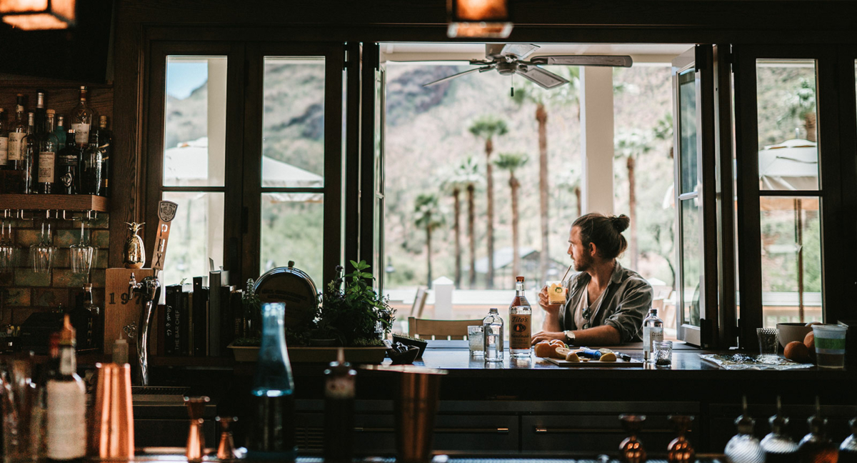a man sitting at a bar with a drink and bottles