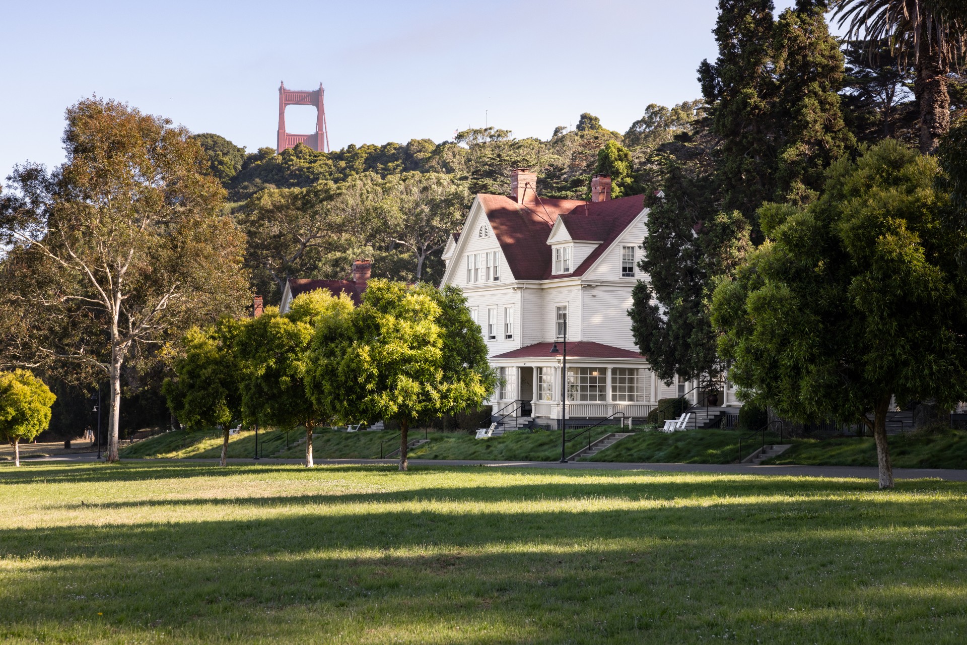 a large white house with a red roof and a large red bridge in the background