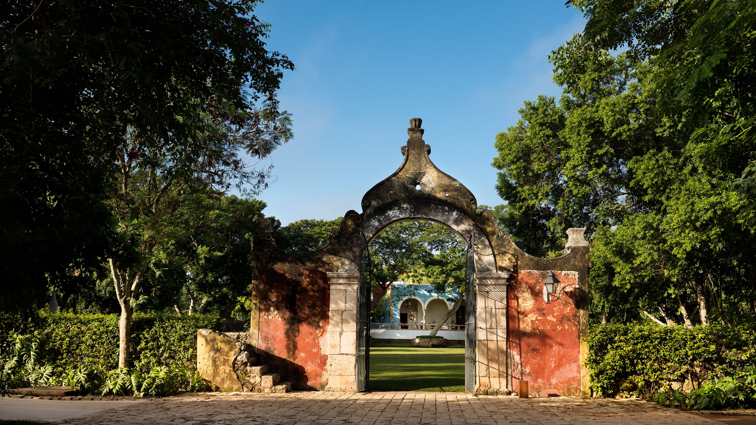 a stone archway with a brick wall and a green lawn