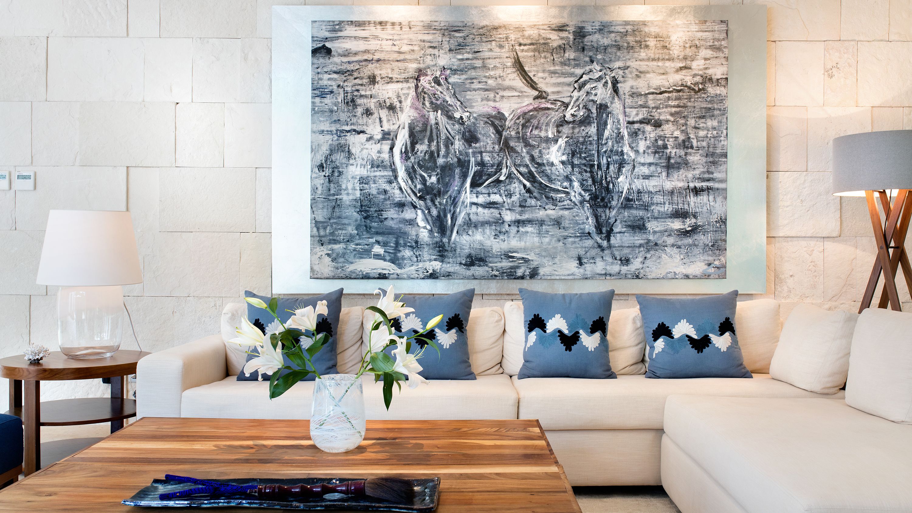 a white couch with blue pillows and a vase with white flowers