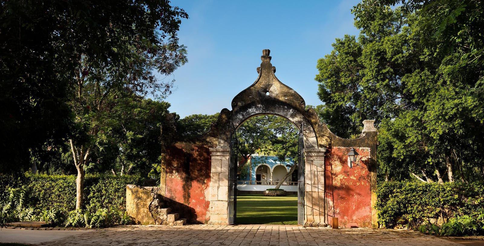 a stone archway with a green lawn and trees