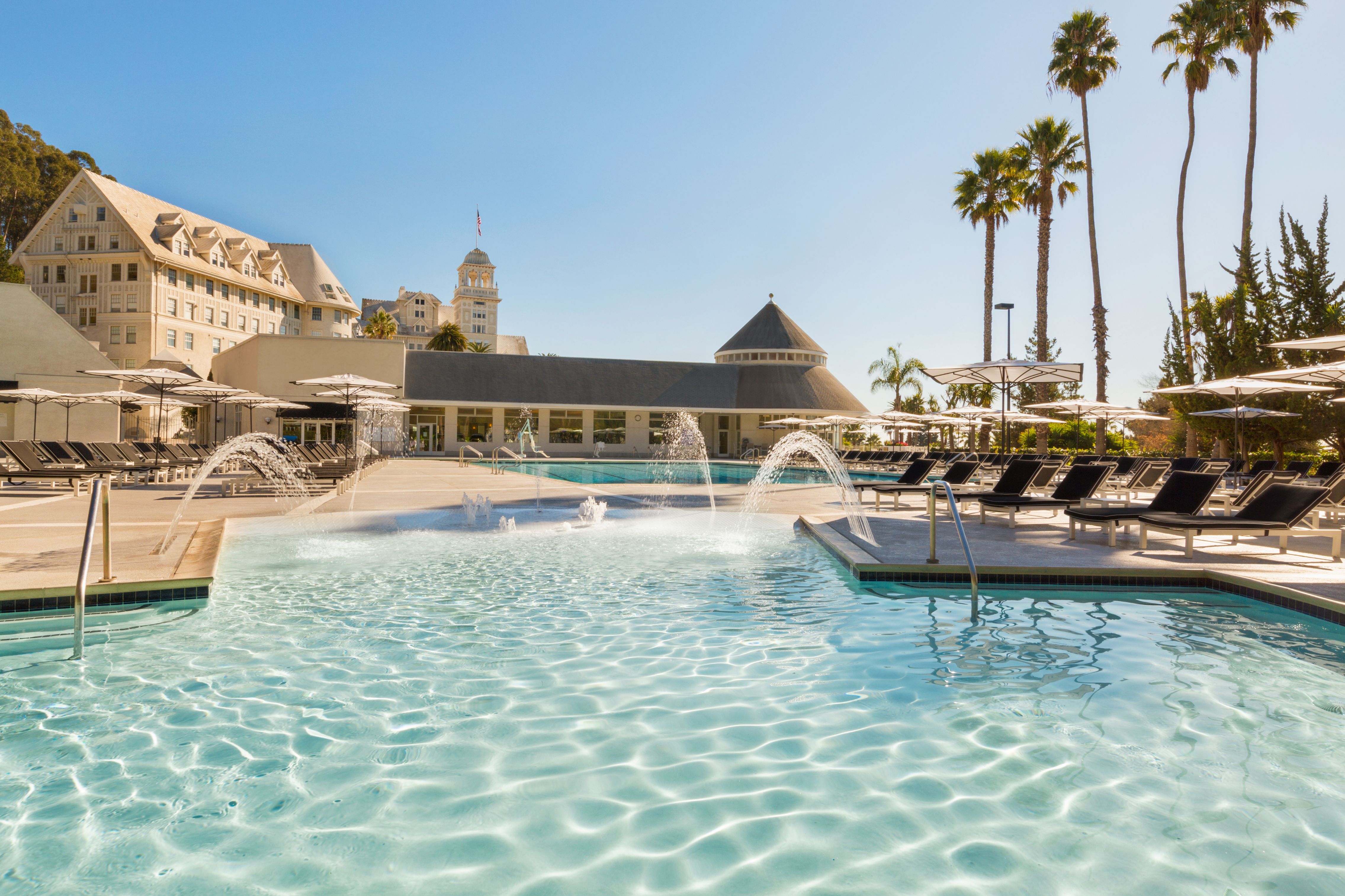 a pool with water jets and umbrellas in front of a building
