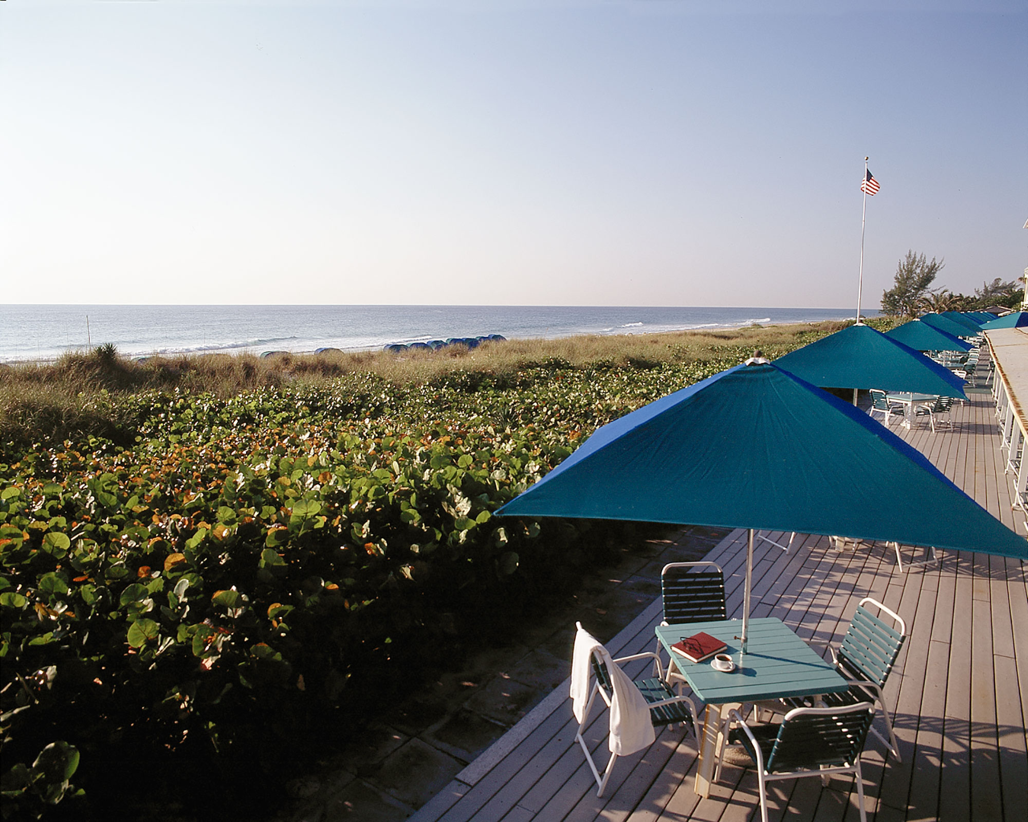 a table and chairs on a deck with a beach and ocean
