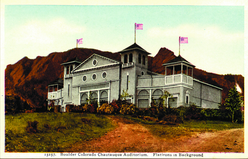 A vintage postcard illustration of the historic Chautauqua Auditorium in Boulder, Colorado, with American flags flying above its towers and the Flatirons mountains rising in the background.