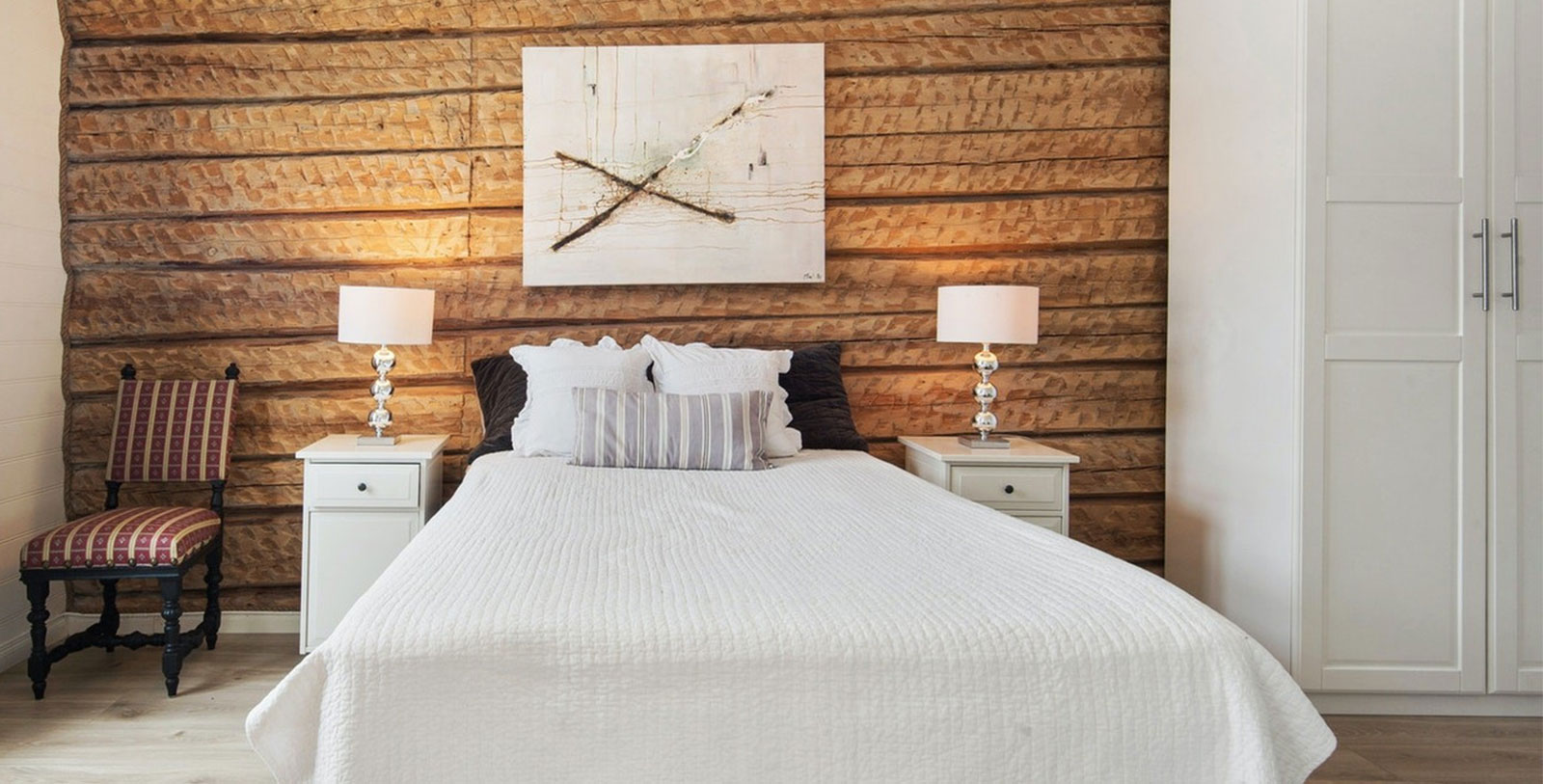 a bed with white bedding and two lamps on a wooden wall