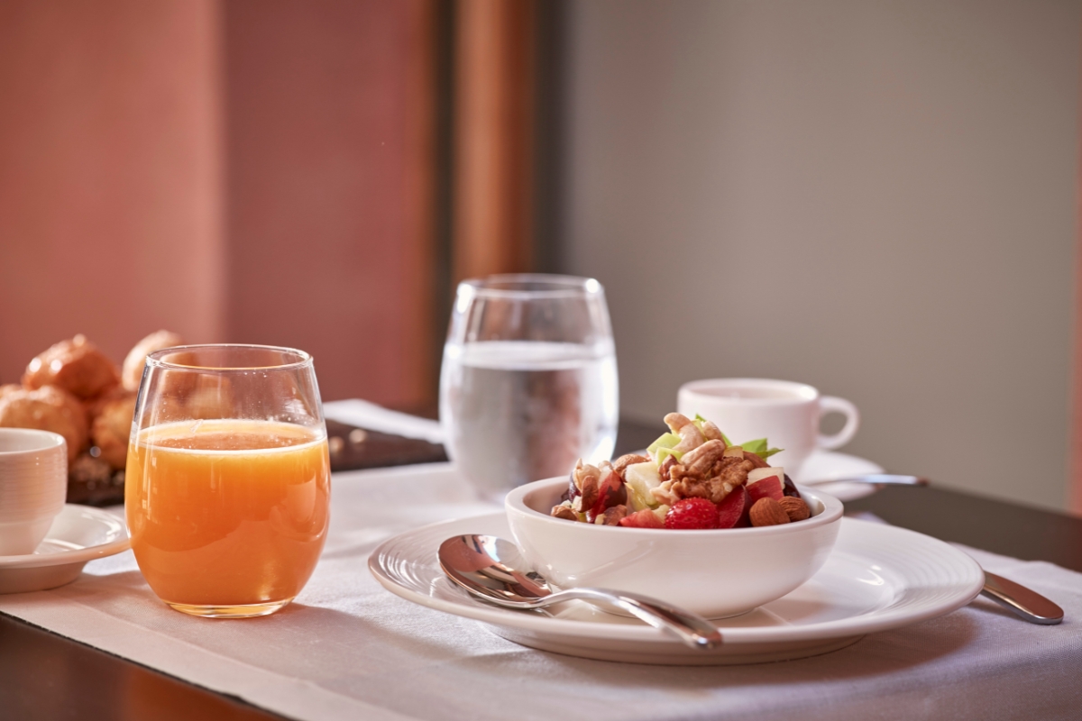 a bowl of fruit and nuts on a plate next to a glass of orange juice