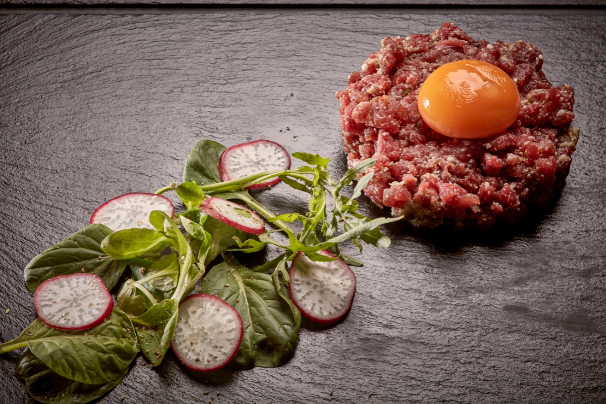 a raw meat tartare with a yolk and a vegetable salad