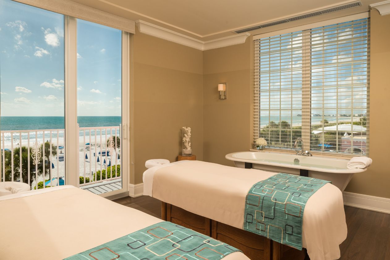 a room with two beds and a tub with a view of the ocean