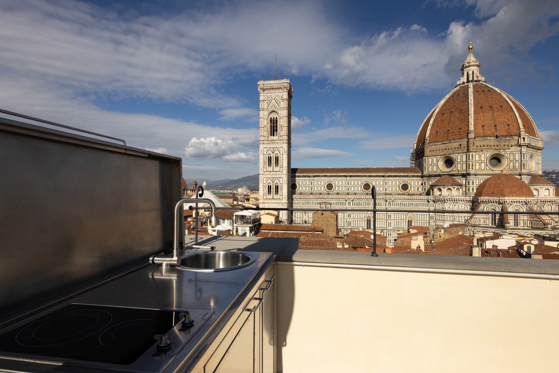 Rooftop terrace with a stainless steel outdoor kitchen station, offering panoramic views of Brunelleschi's Dome and Giotto's Campanile in Florence, Italy.