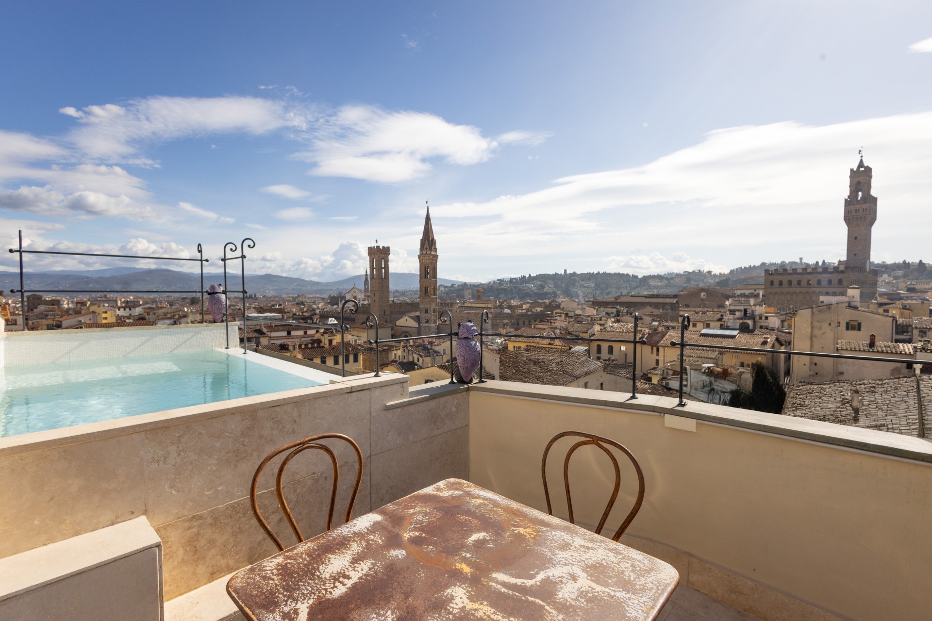 Rooftop terrace featuring a small plunge pool, a distressed metal table with chairs, and sweeping views of the Florence skyline including Palazzo Vecchio and Badia Fiorentina.