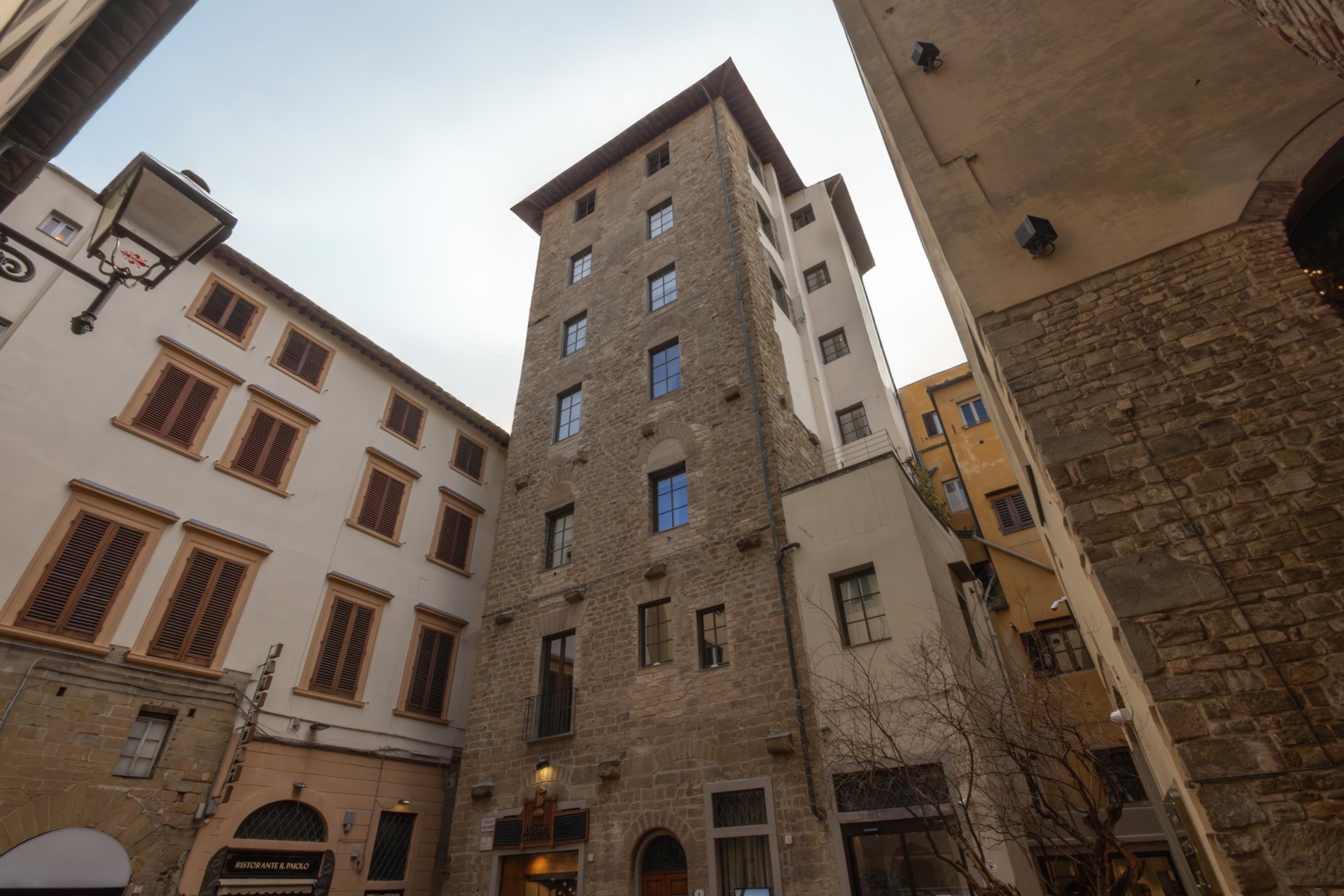 Low-angle view of a historic stone tower building nestled in a narrow Florentine alleyway, surrounded by traditional Tuscan architecture.