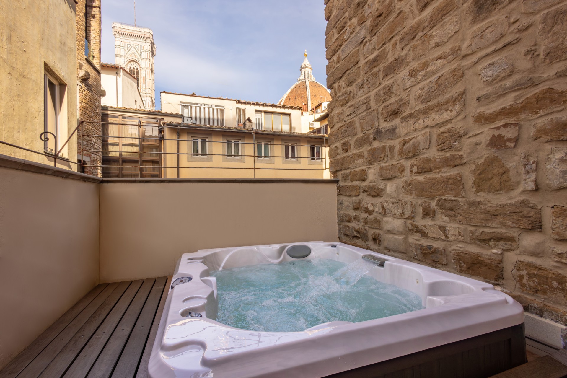 Outdoor private balcony terrace with a white jacuzzi tub and a view of the Florence Cathedral (Duomo) and Giotto's Campanile in the background.
