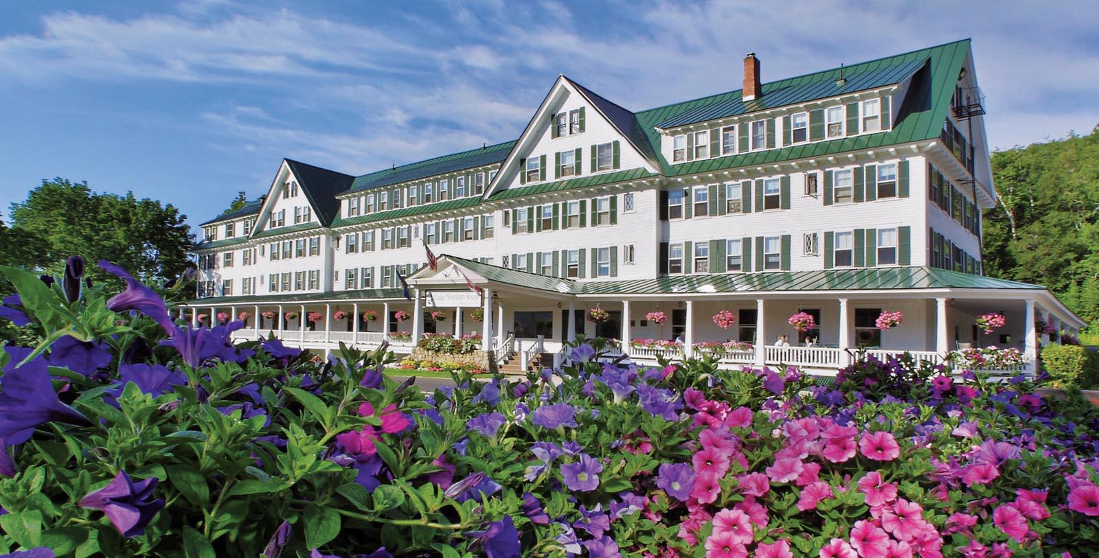 a large white building with green roof and purple flowers 