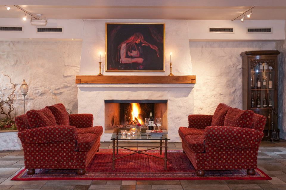 a fireplace with red chairs and a painting above it