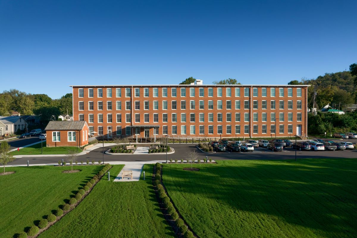 a large brick building with a parking lot and grass with Hampton Court Palace in the background