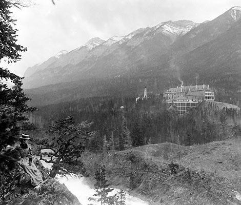 a woman sitting on a rock looking at a building in the mountains