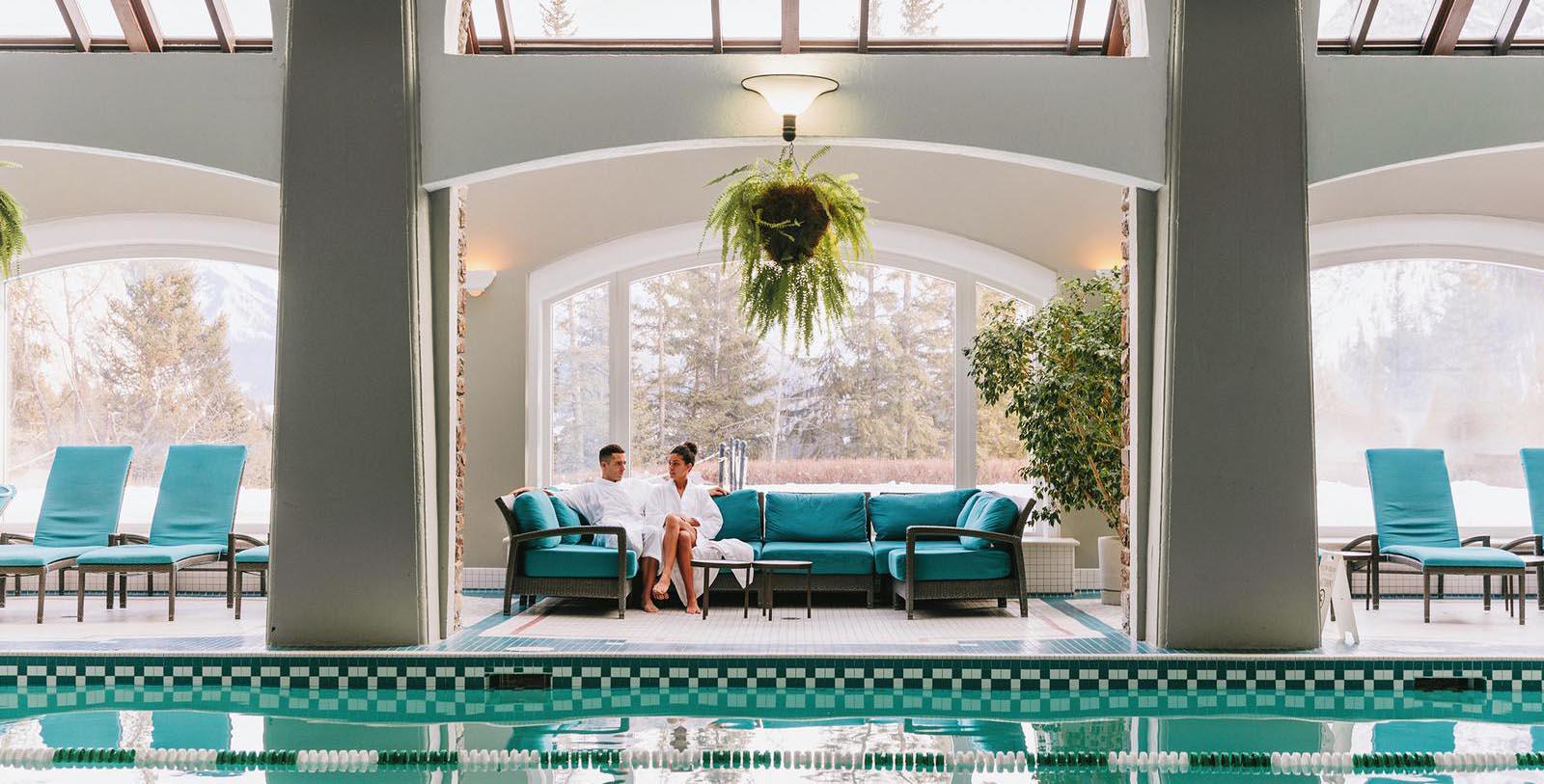 a man and woman sitting on a couch in a room with a pool