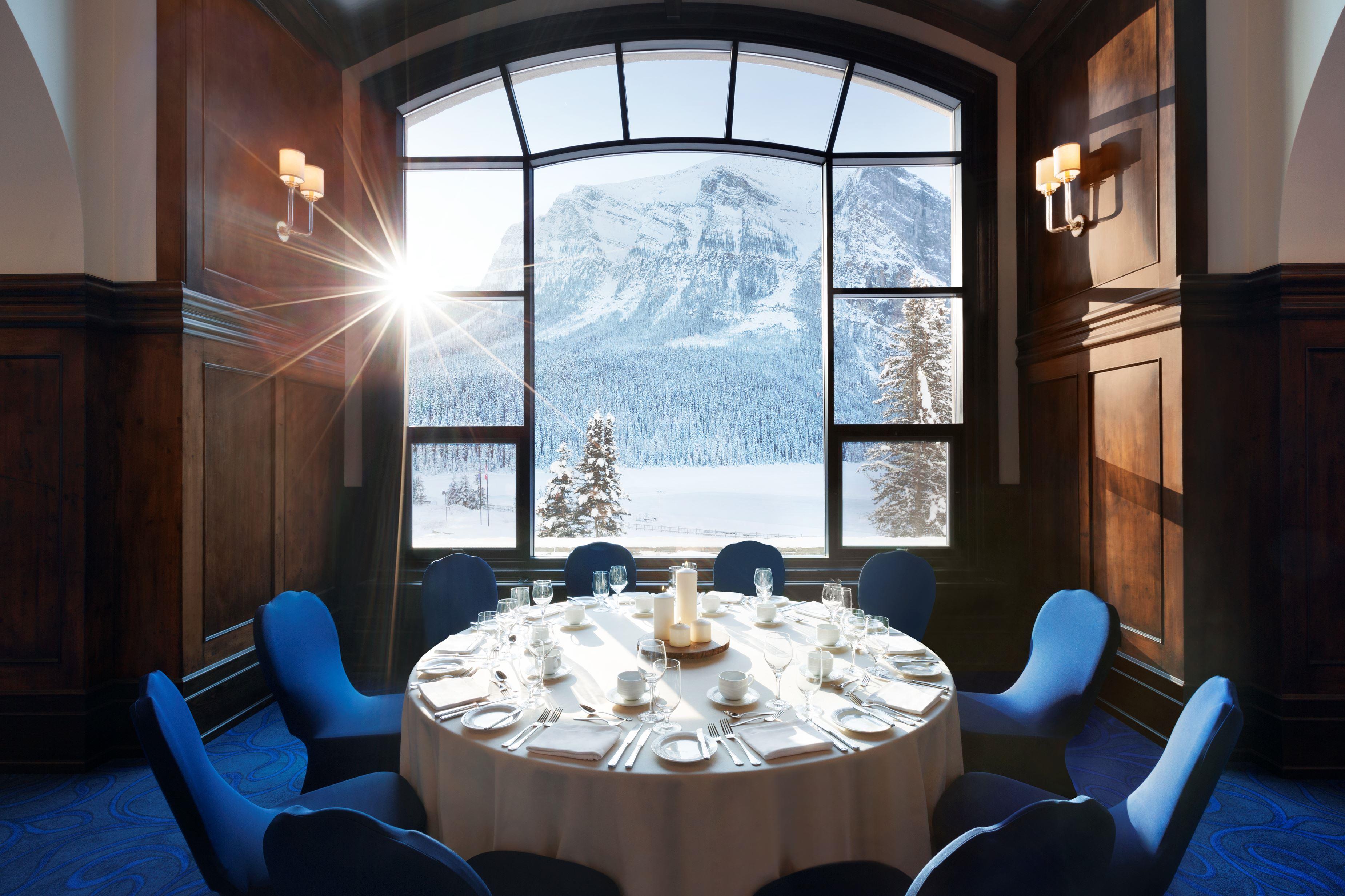 a room with a round table and chairs and a view of a snowy mountain