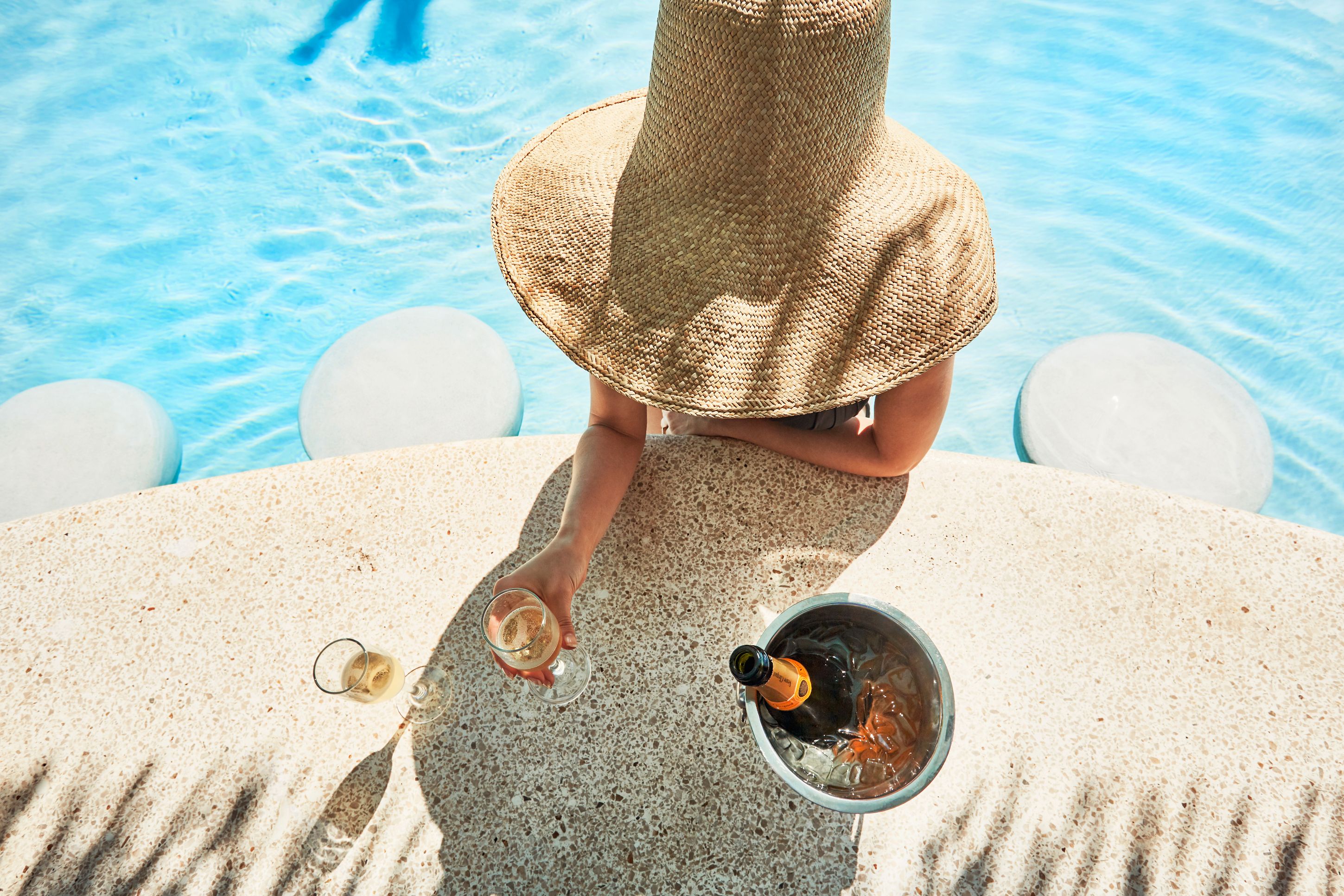 a person wearing a hat and holding glasses of wine