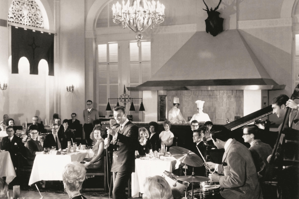 a man singing into a microphone in a room with people in the background