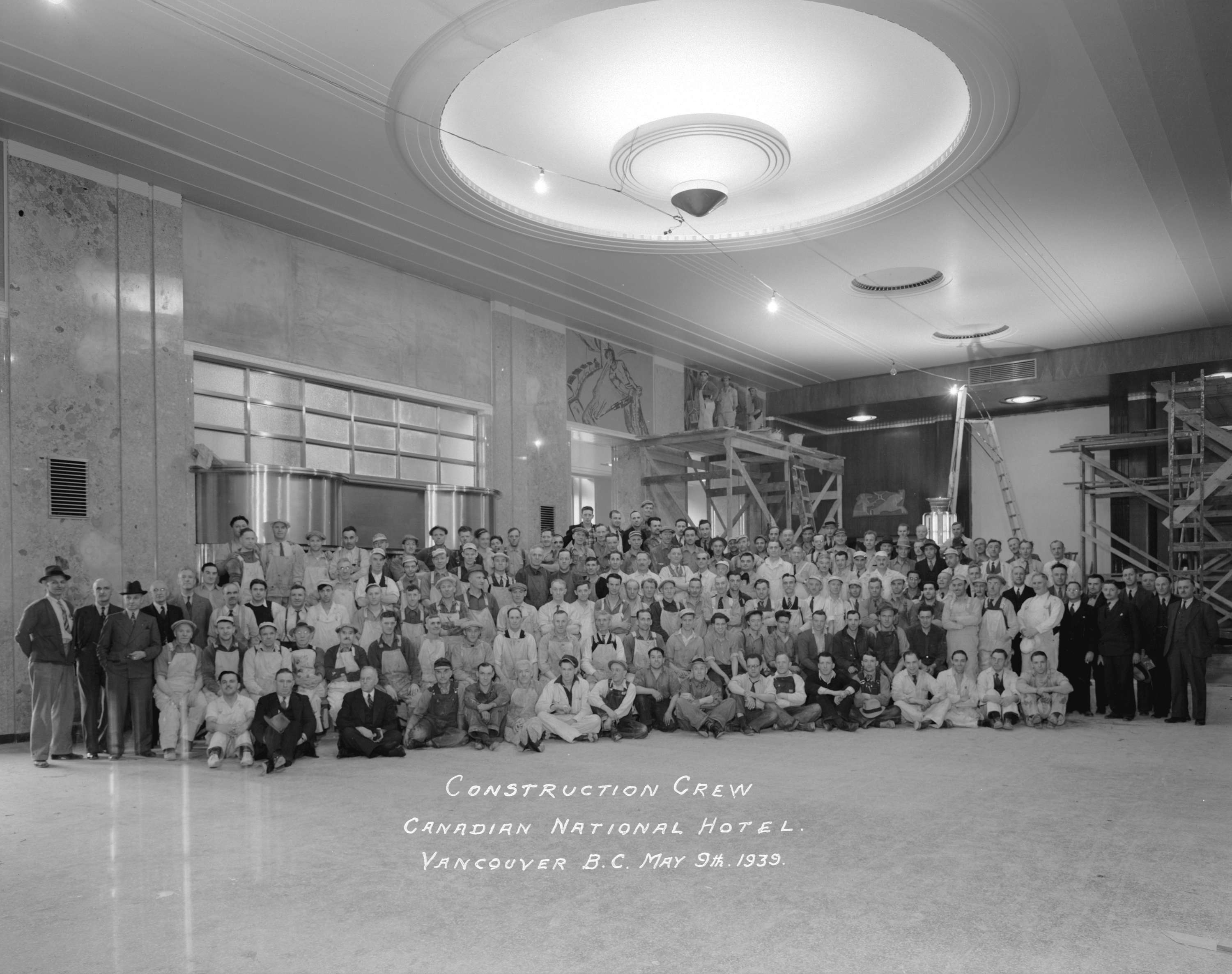 A historic black and white group photo of a large construction crew posing inside the Canadian National Hotel in Vancouver, B.C., dated May 9th, 1939.