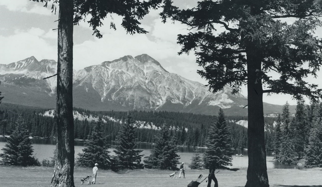 a group of people playing golf in a field with trees and a mountain in the background