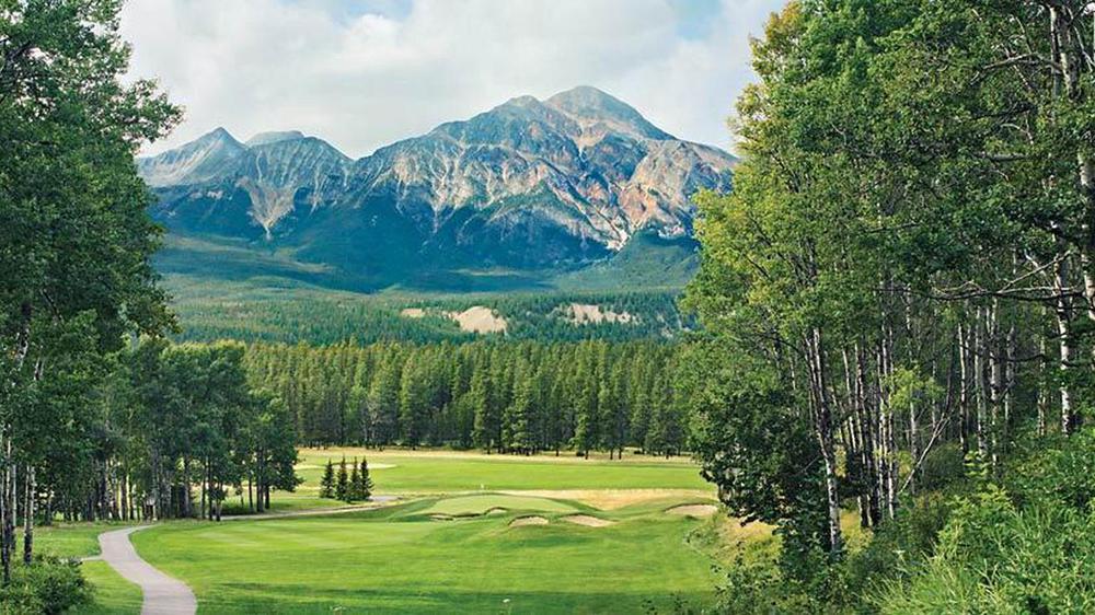 a golf course with trees and mountains in the background