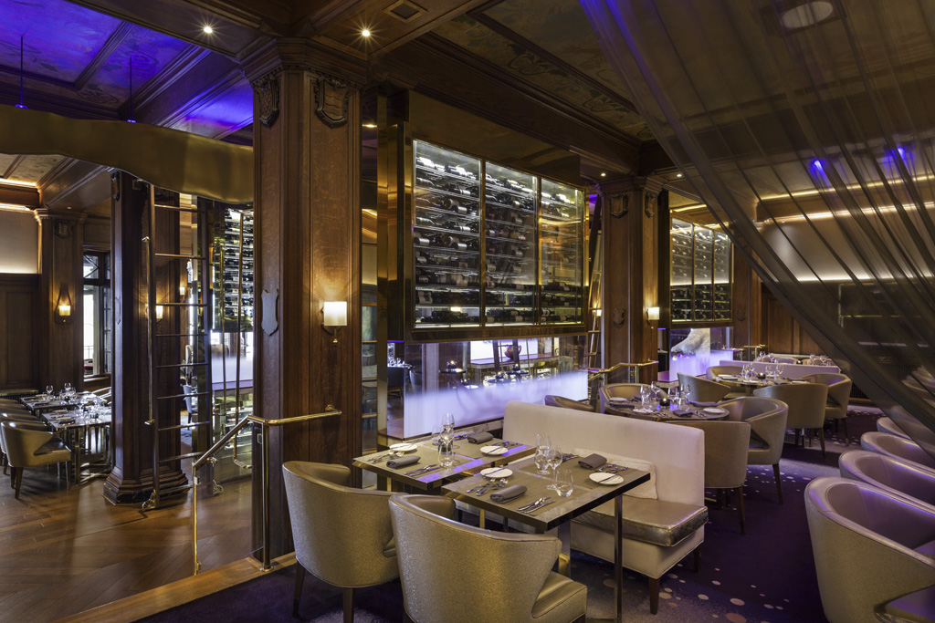 The original paneling and stenciled ceilings are preserved while a palette of luxurious textured materials such as leather, wood, and brass in muted hues of purple, grey, and beige keep the space contemporary.