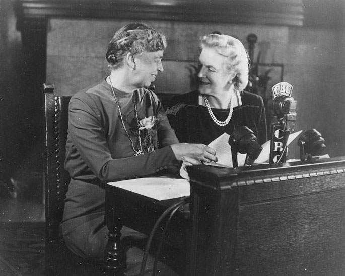 a woman sitting at a desk with a microphone and smiling