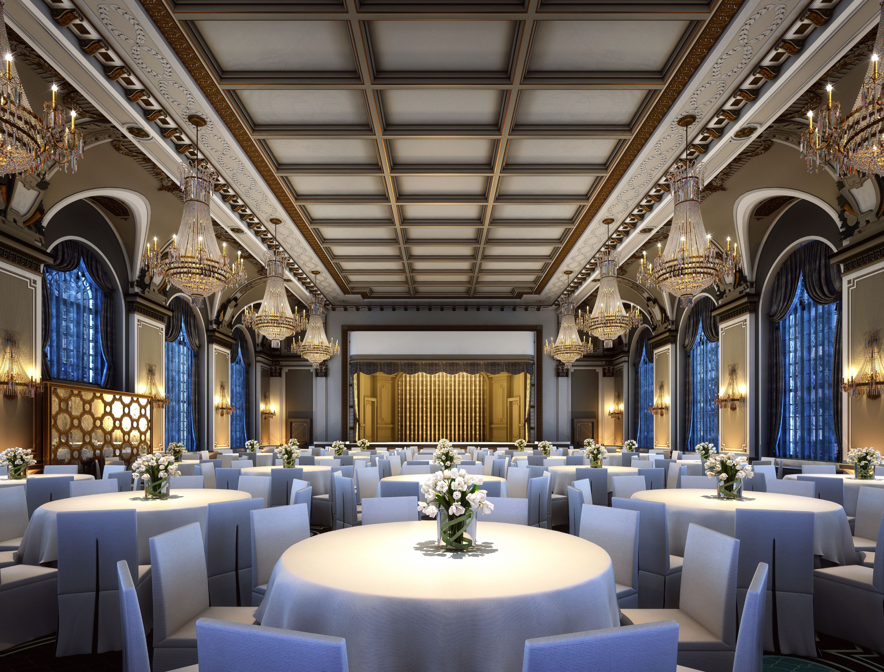 Grand, ornate ballroom set up for an event, featuring round dining tables with white linens, crystal chandeliers, a coffered ceiling, and an elevated stage at the far end.